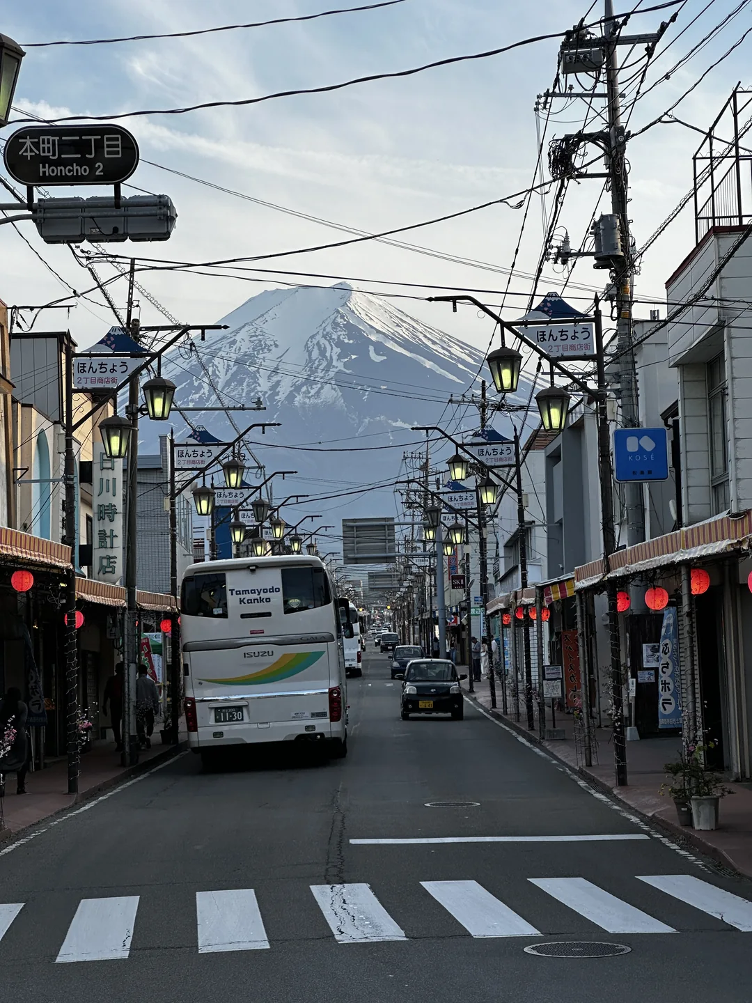 Gunung Fuji terlihat di ujung jalan kota dengan pertokoan dan penyeberangan