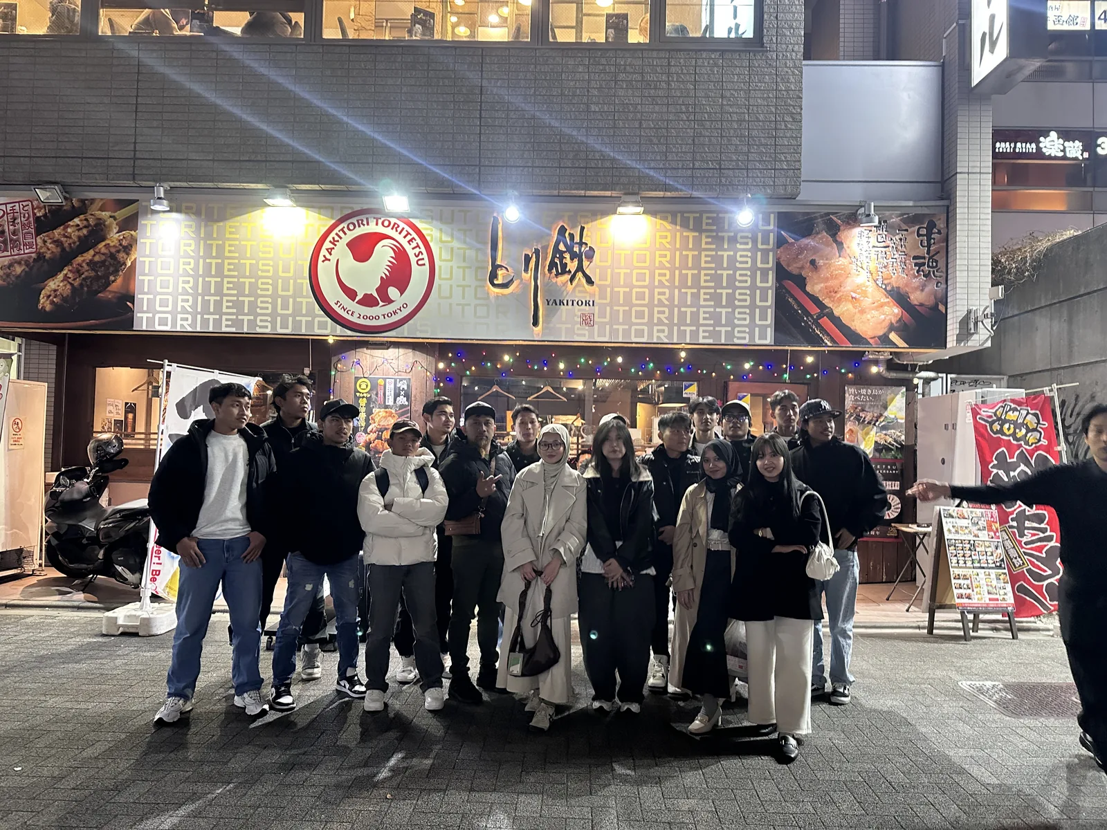 Sekelompok orang berfoto bersama di depan bangunan yang terang pada malam hari