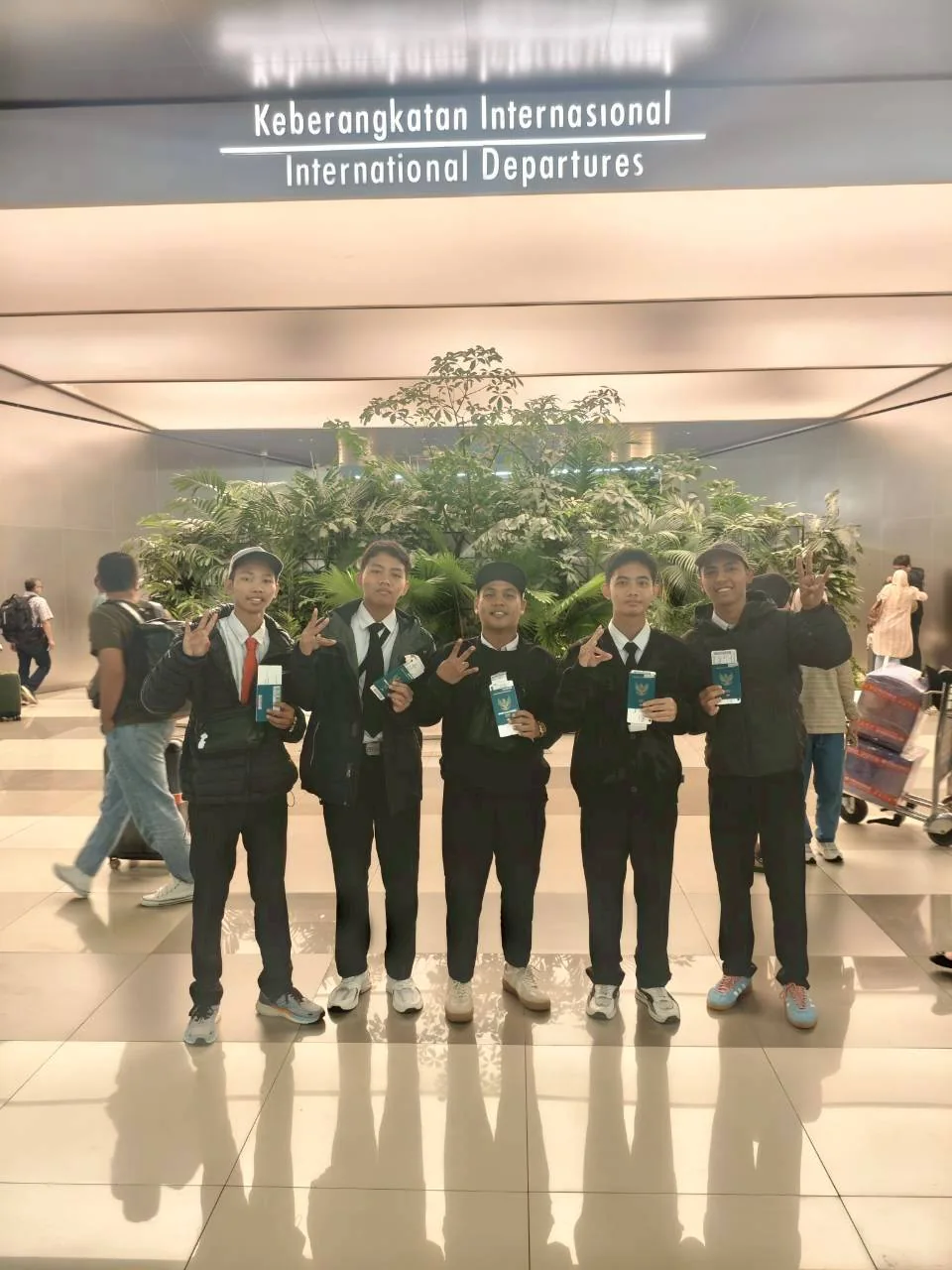 Lima siswa berfoto bersama di bawah papan keberangkatan internasional